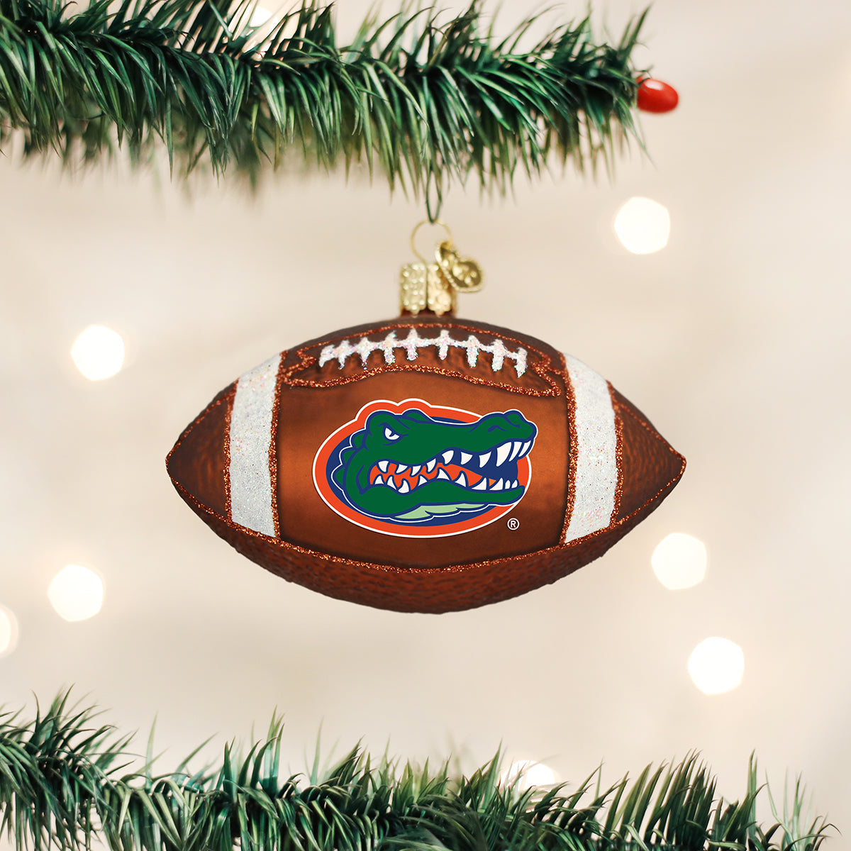 Brown glass football ornament featuring the Florida Gators logo, white glitter laces, and hanging on a pine branch.