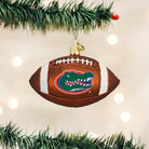 Brown glass football ornament featuring the Florida Gators logo, white glitter laces, and hanging on a pine branch.