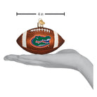 4-inch brown glass Florida Gators football ornament with white laces and team logo, held in a hand.