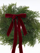 Mini faux cedar Christmas cabinet wreath featuring a deep red velvet ribbon bow on a white background.