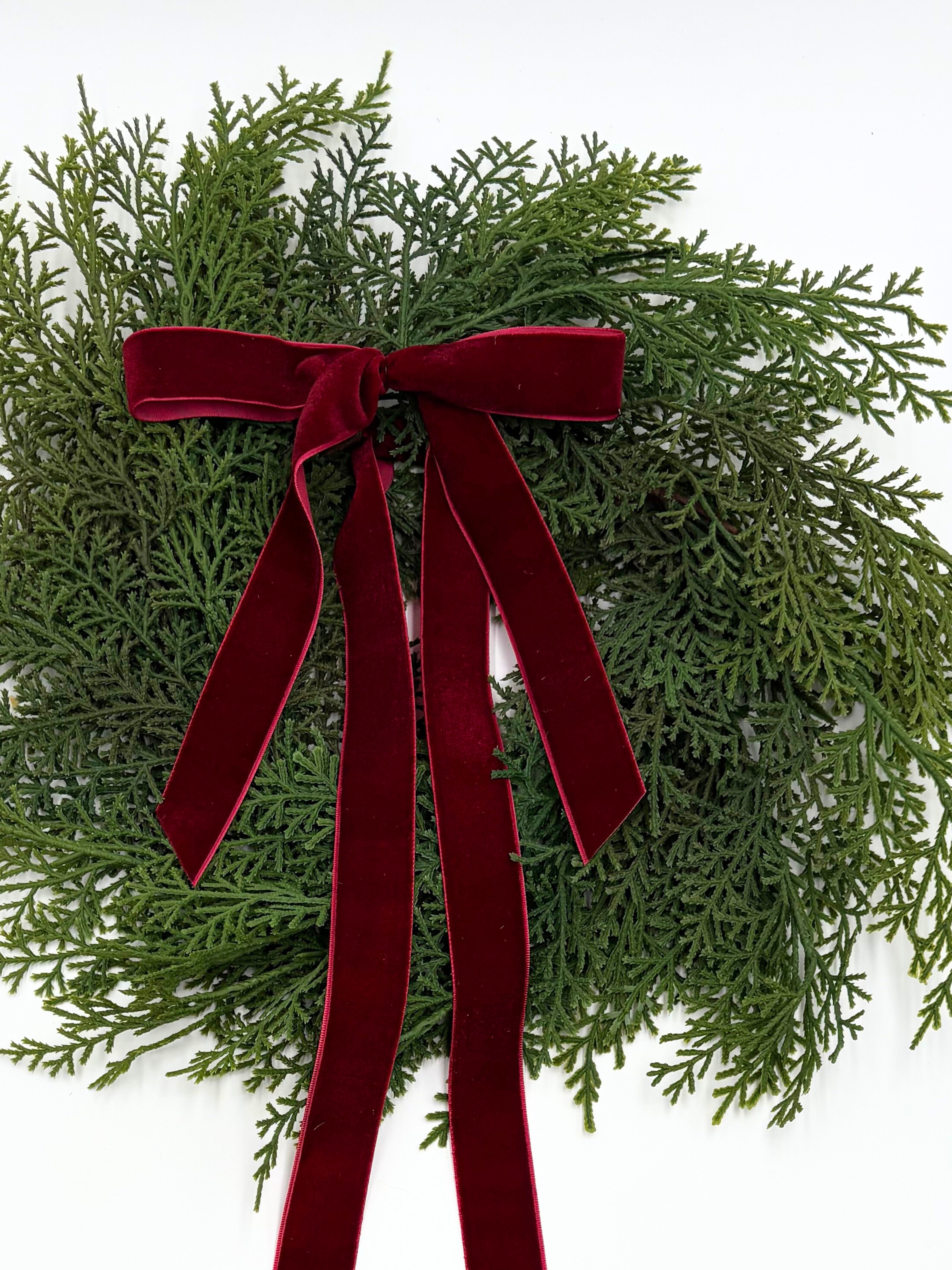 Mini faux cedar Christmas cabinet wreath featuring a deep red velvet ribbon bow on a white background.