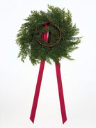 Mini Christmas cabinet wreath made of faux green cedar on a twig base with long, elegant red ribbon streamers.