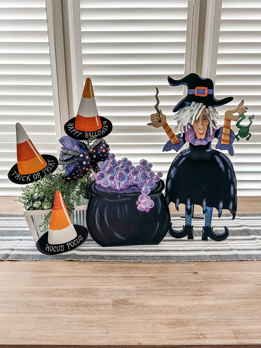 Tillie Cauldron Halloween decor featuring a black pot with purple bubbles, a witch, and candy corn accents on a table.