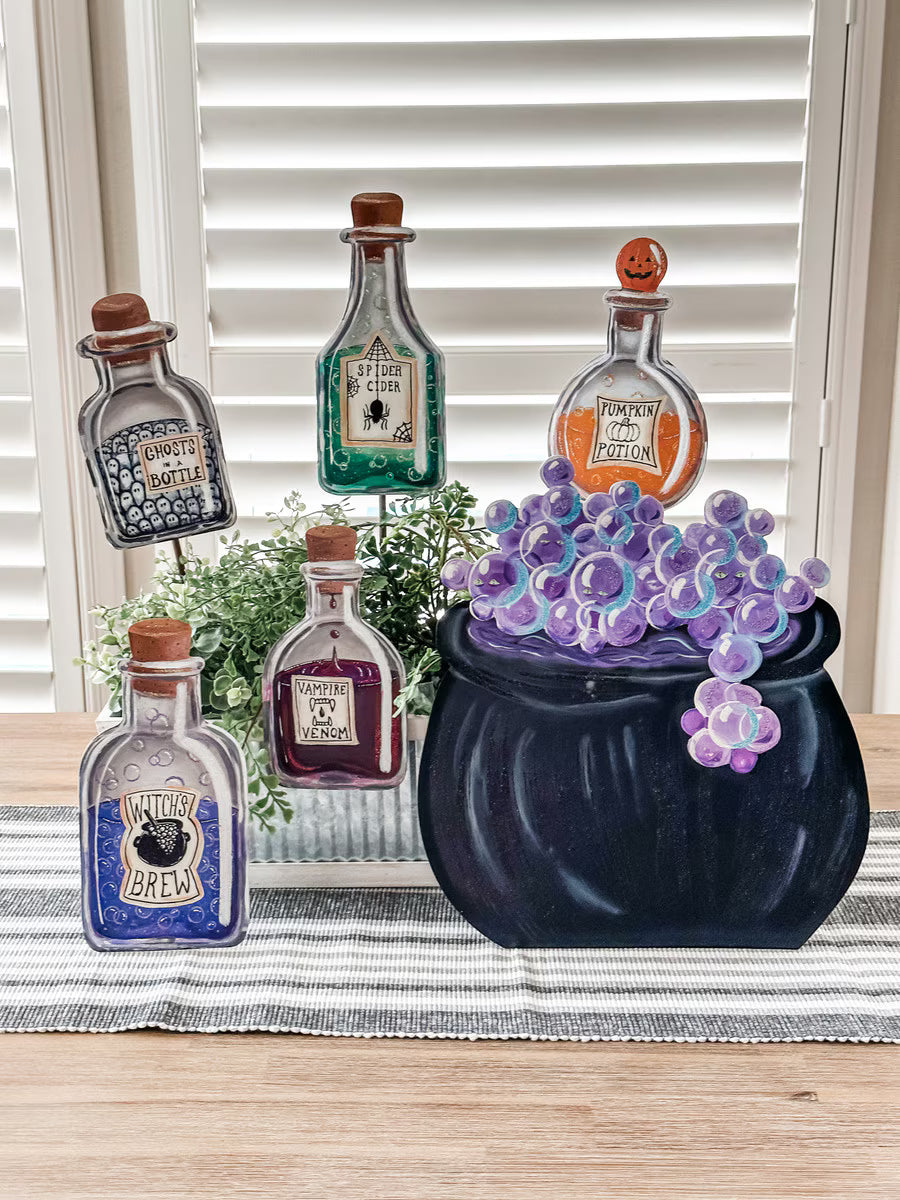 Black witch cauldron with purple bubbles and decorative potion bottle stakes for Halloween seasonal tabletop decor.