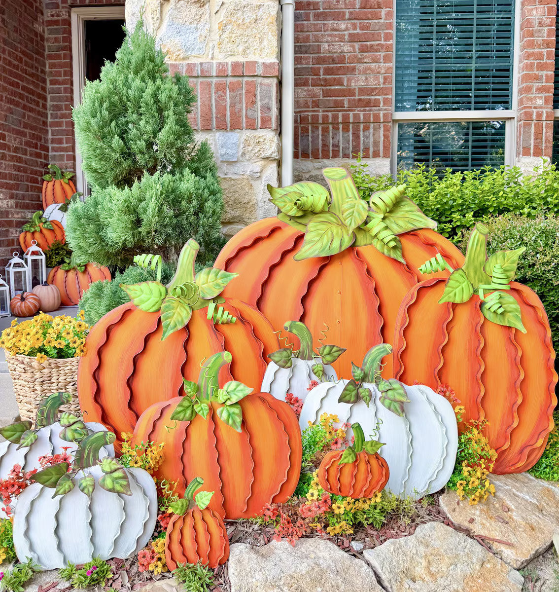 Oversized orange and white metal ribbon pumpkins with green leaves, arranged as a festive fall porch display.