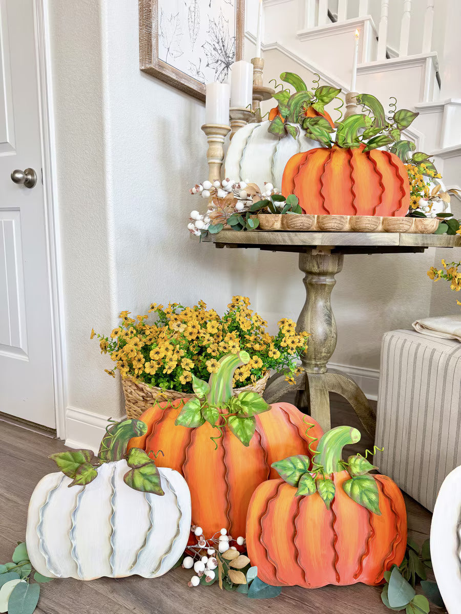 Set of three orange and white ribbon-style metal pumpkins with green leaf accents, displayed as festive autumn home decor.