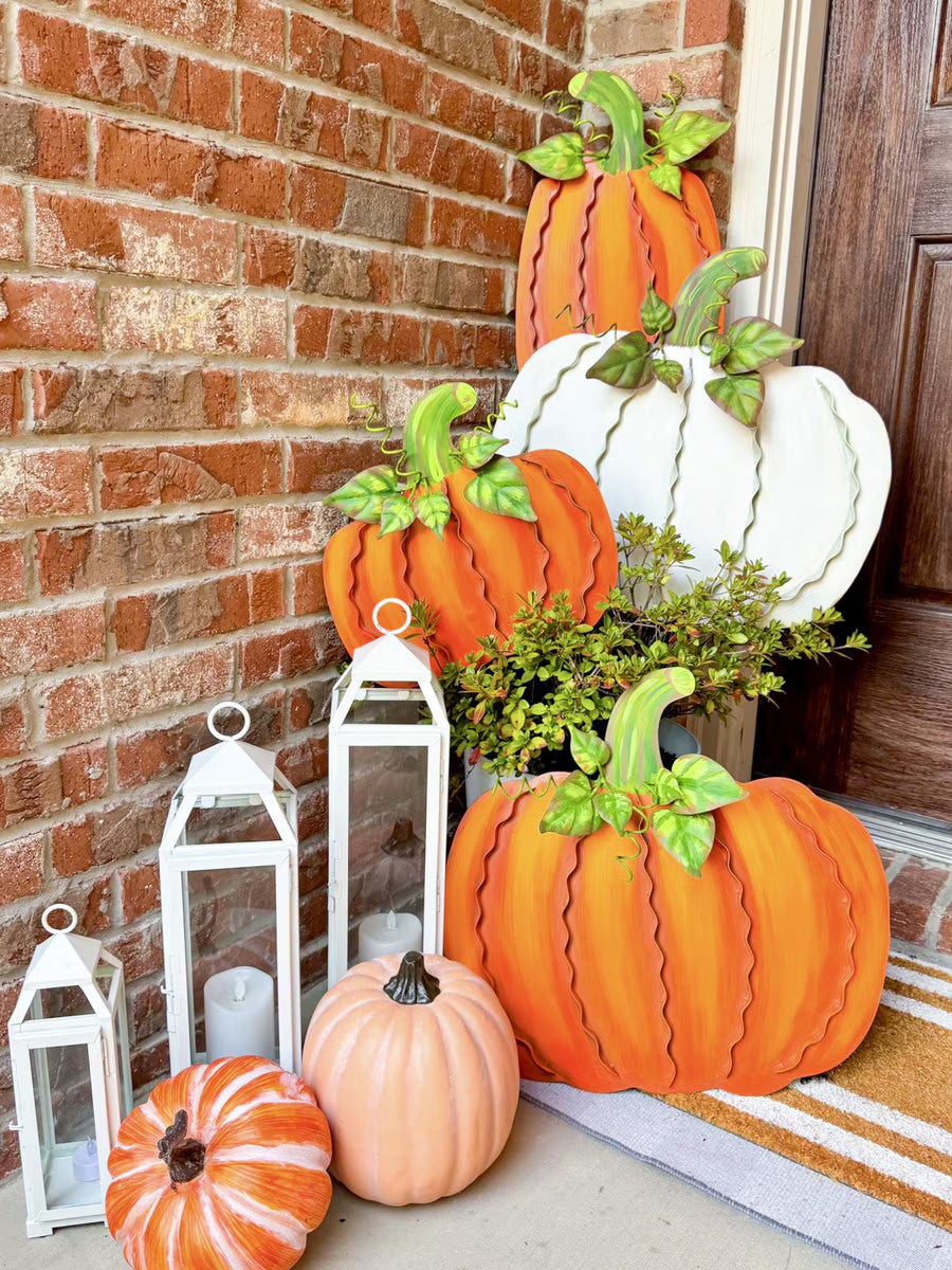 Set of three orange ribbon-detailed metal pumpkins with green stems, displayed as fall porch decor with lanterns.