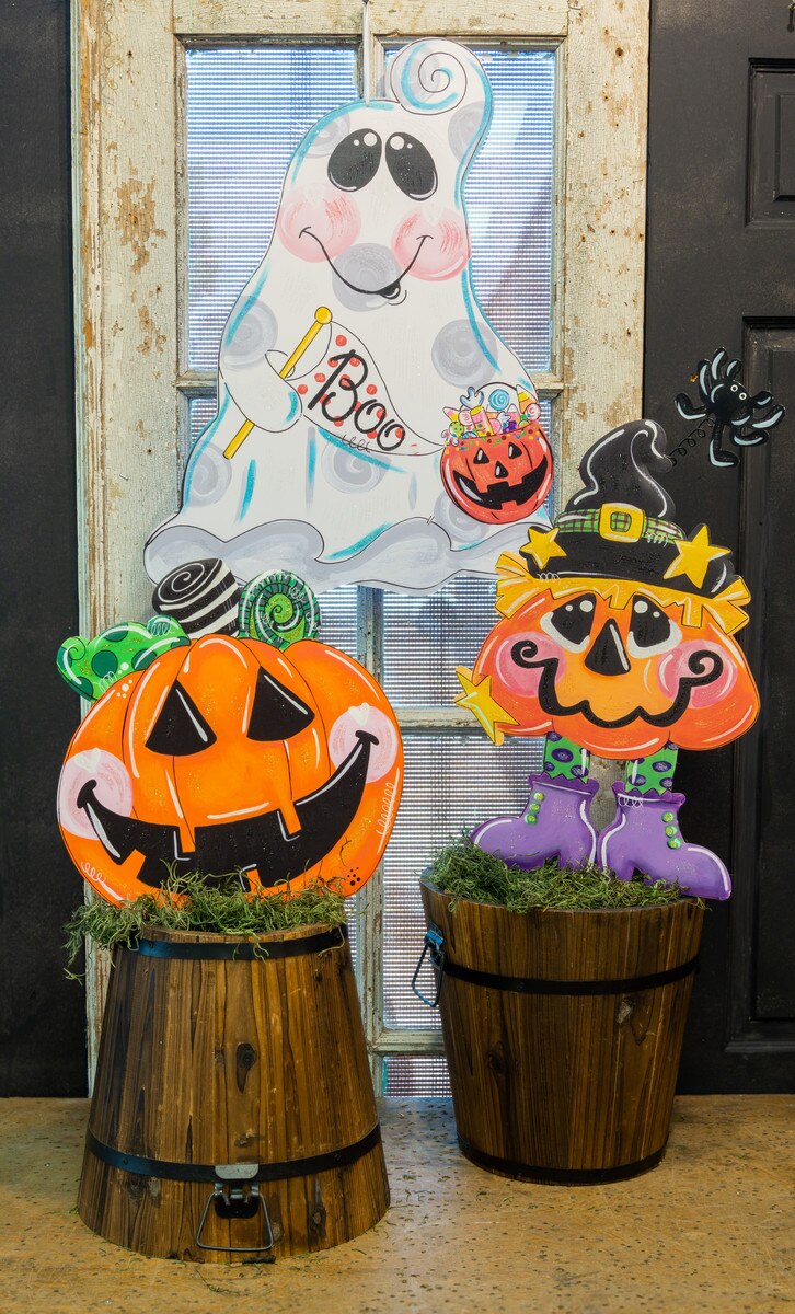 Cheerful 24-inch PVC ghost door hanger with Boo sign and candy bucket, displayed with Halloween pumpkin and witch decor.