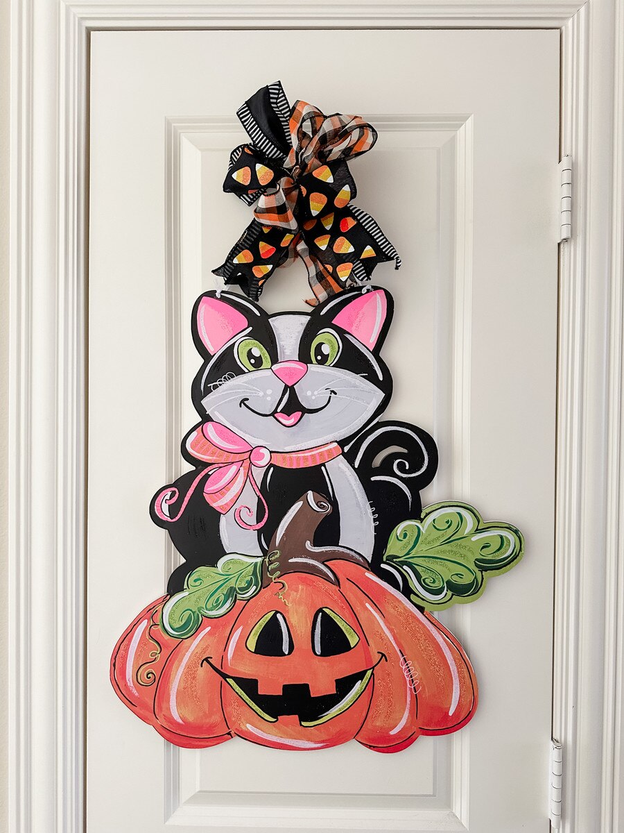 Black cat and jack-o'-lantern PVC Halloween door hanger with a festive candy corn bow, 24 inches tall.