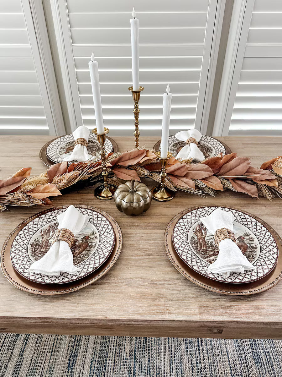 72-inch wheat and dried leaf garland centerpiece on a rustic dining table with brass candlesticks and autumn place settings.