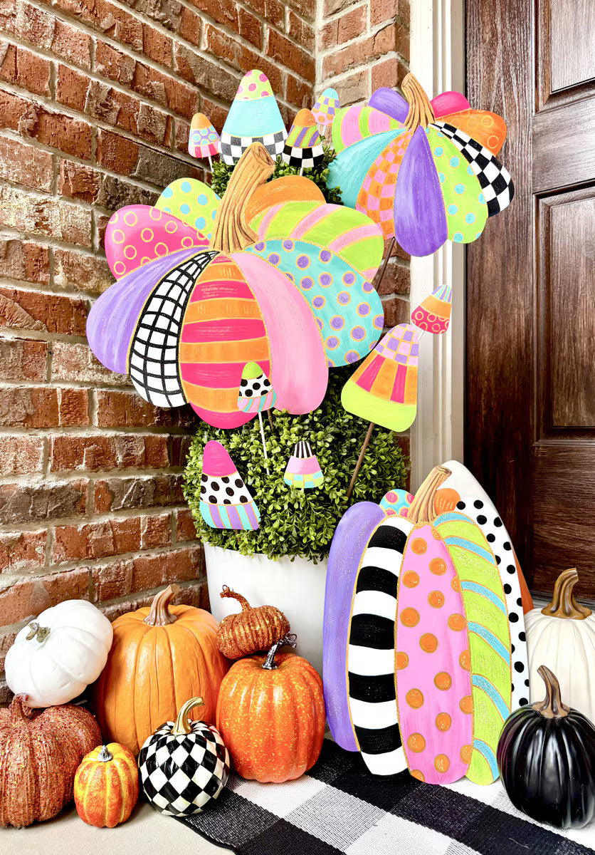 Colorful patterned pumpkin stakes with polka dots and stripes, displayed in a planter with assorted decorative pumpkins.