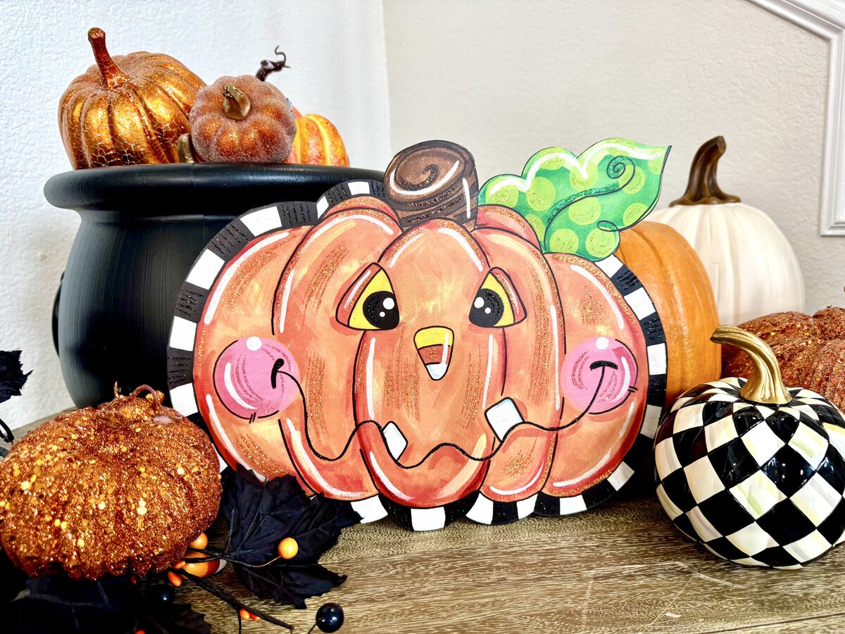 Whimsical 13-inch orange jack-o'-lantern cutout with a candy corn nose, black and white striped trim, and green leaf.
