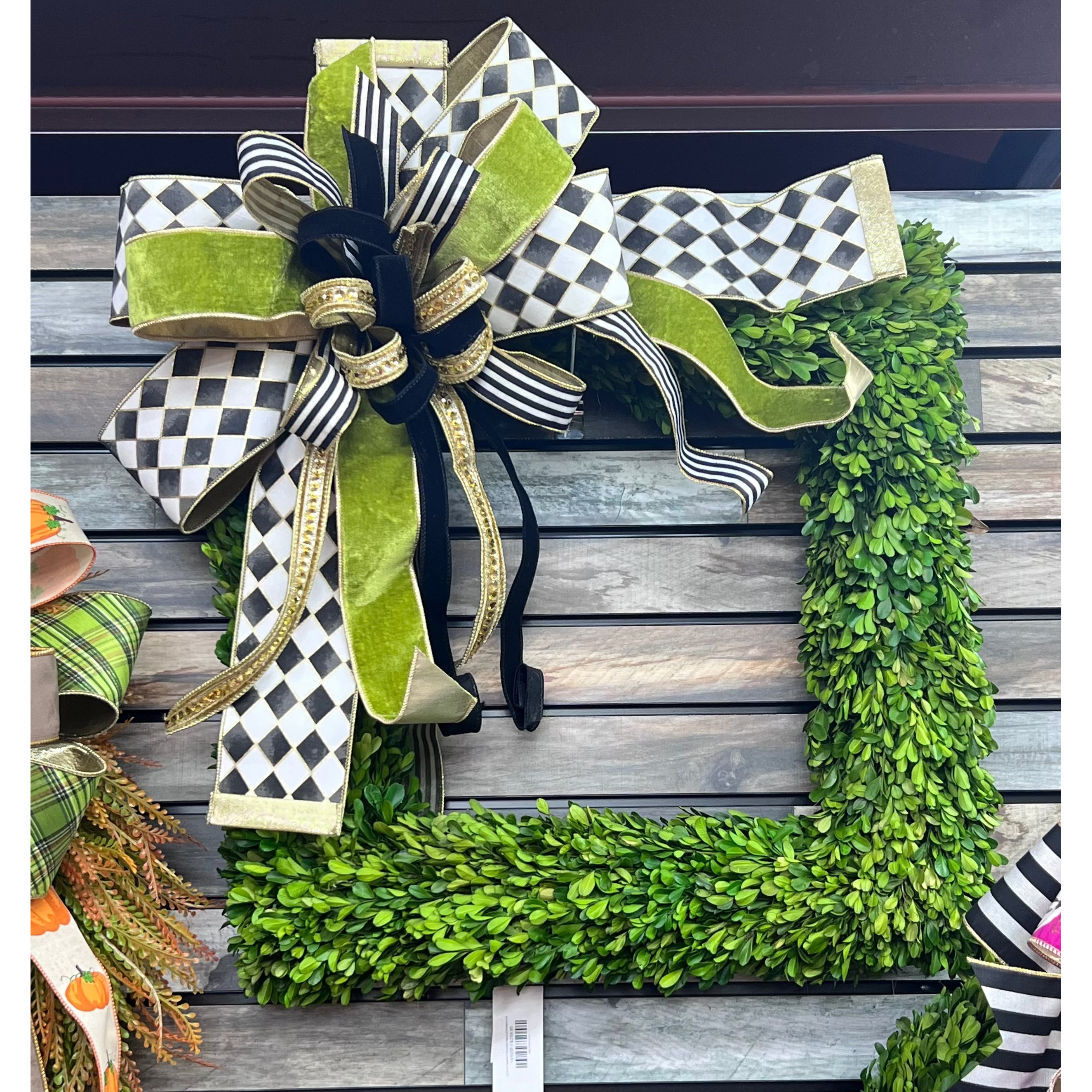Large decorative bow featuring black and white checkered ribbon, lime green velvet, and gold accents on a boxwood wreath.