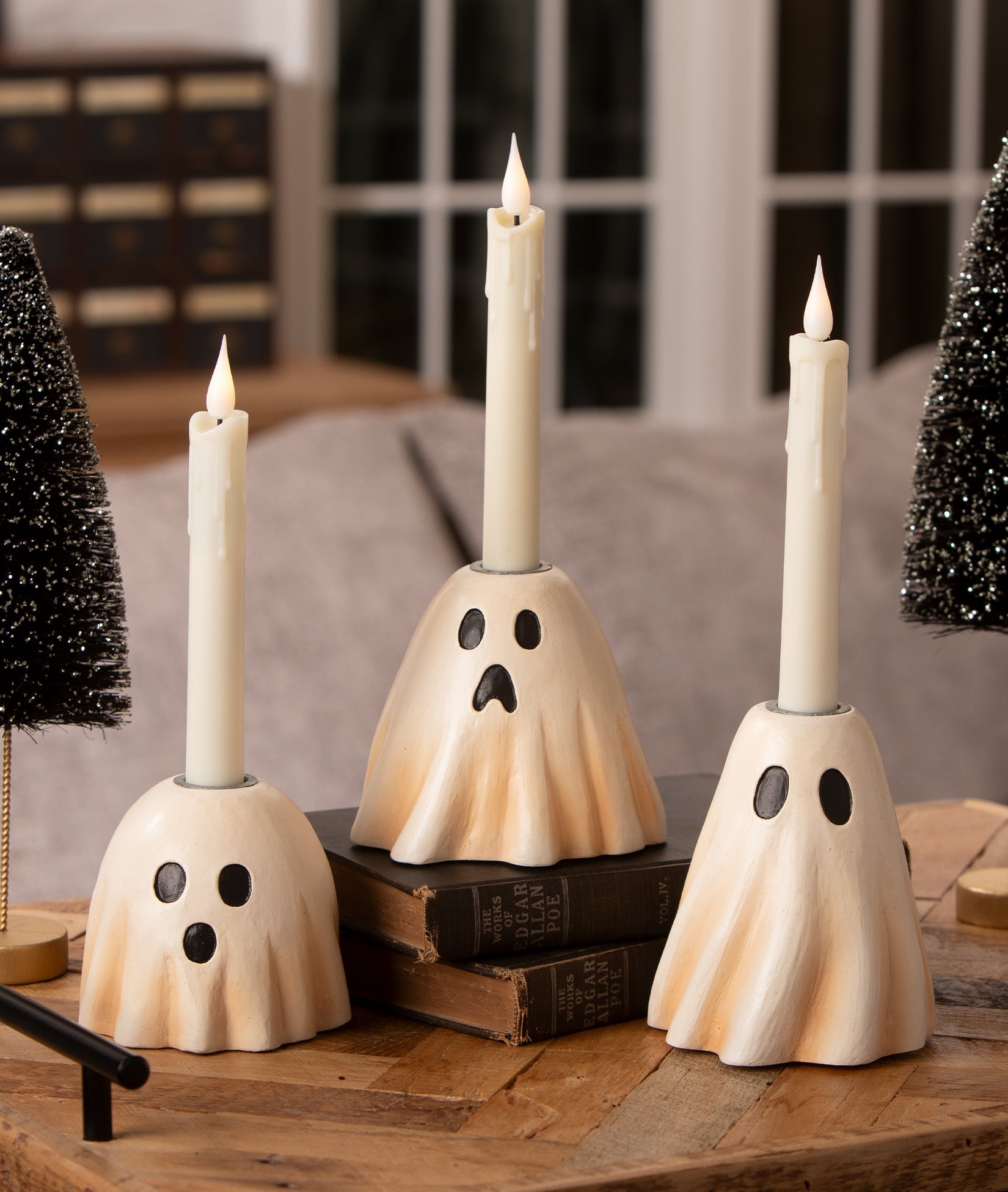 Three vintage-style cream resin ghost candlesticks with black eyes and mouths, each holding a white taper candle.