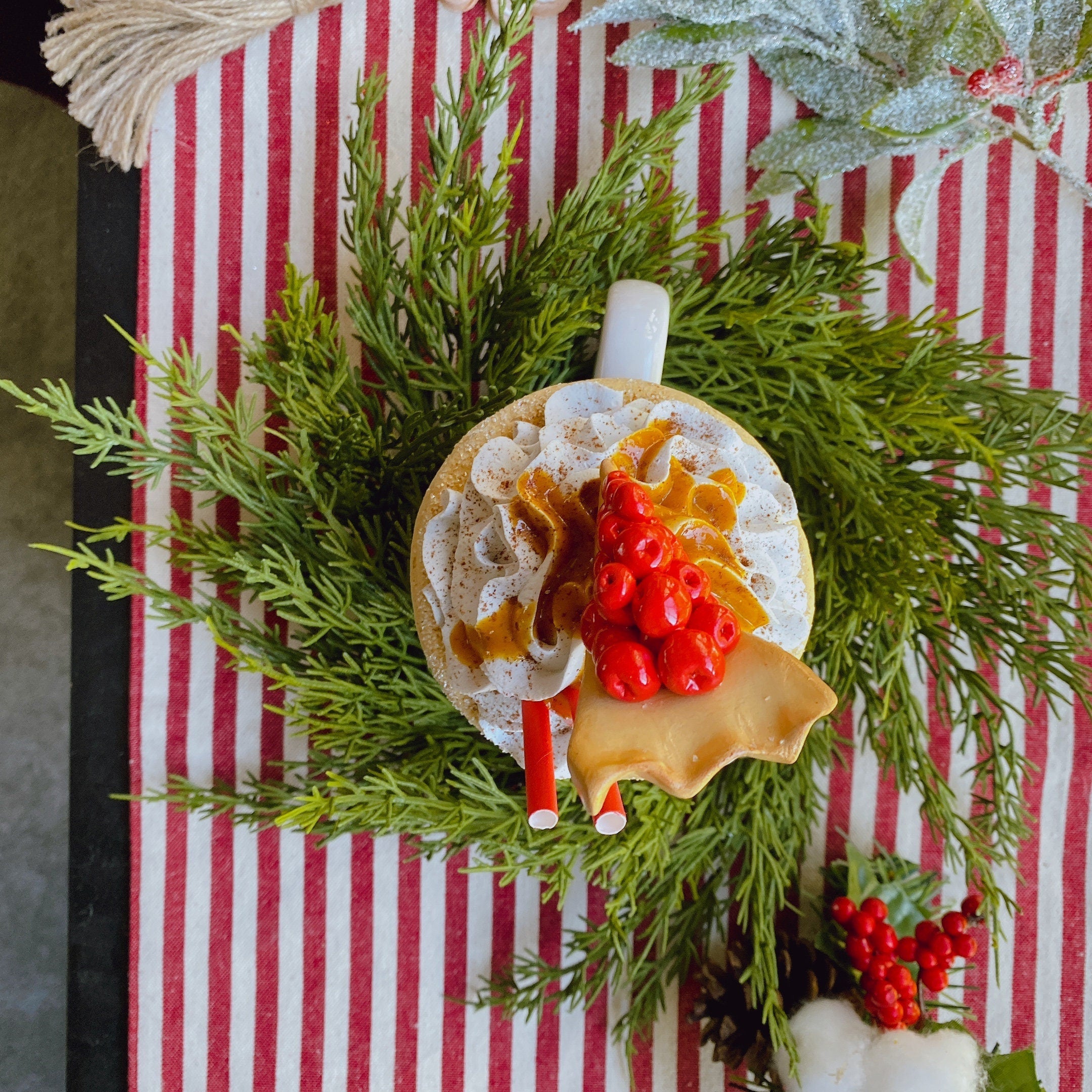 14-inch faux cedar mini Christmas wreath surrounding a festive mug on a red and white striped table runner.