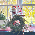 14-inch faux cedar mini Christmas wreath with realistic green foliage, styled as farmhouse holiday decor on a window sill.