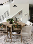 Mini faux cedar wreaths with caramel velvet ribbons hanging on wooden dining chairs in a farmhouse-style dining room.