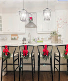 Mini artificial cedar Christmas wreaths with bright red bows hanging on black kitchen bar stools and cabinets.