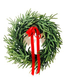 Lifelike Norfolk pine winter wreath with lush green needles and a festive red velvet ribbon bow.