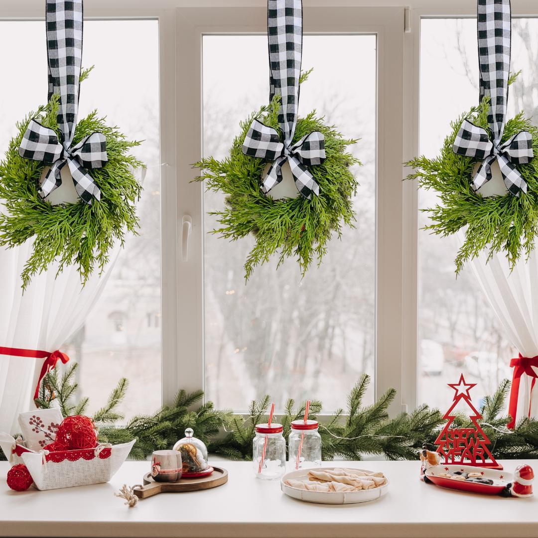 Three mini artificial cedar wreaths with black and white buffalo check ribbons hanging on a window for Christmas.