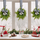Three mini artificial cedar wreaths with black and white buffalo check ribbons hanging on a window for Christmas.