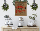 Two mini artificial cedar wreaths with black and white buffalo check ribbons hanging above a coffee station.