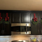 Mini artificial cedar Christmas wreaths with red and black buffalo plaid ribbon hanging on dark kitchen cabinets.