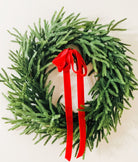 Lifelike Real Touch Norfolk Pine winter wreath with lush green needles and a vibrant red velvet ribbon bow.
