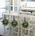 Mini artificial cedar wreaths with black and white buffalo check bows hanging on white dining chairs.