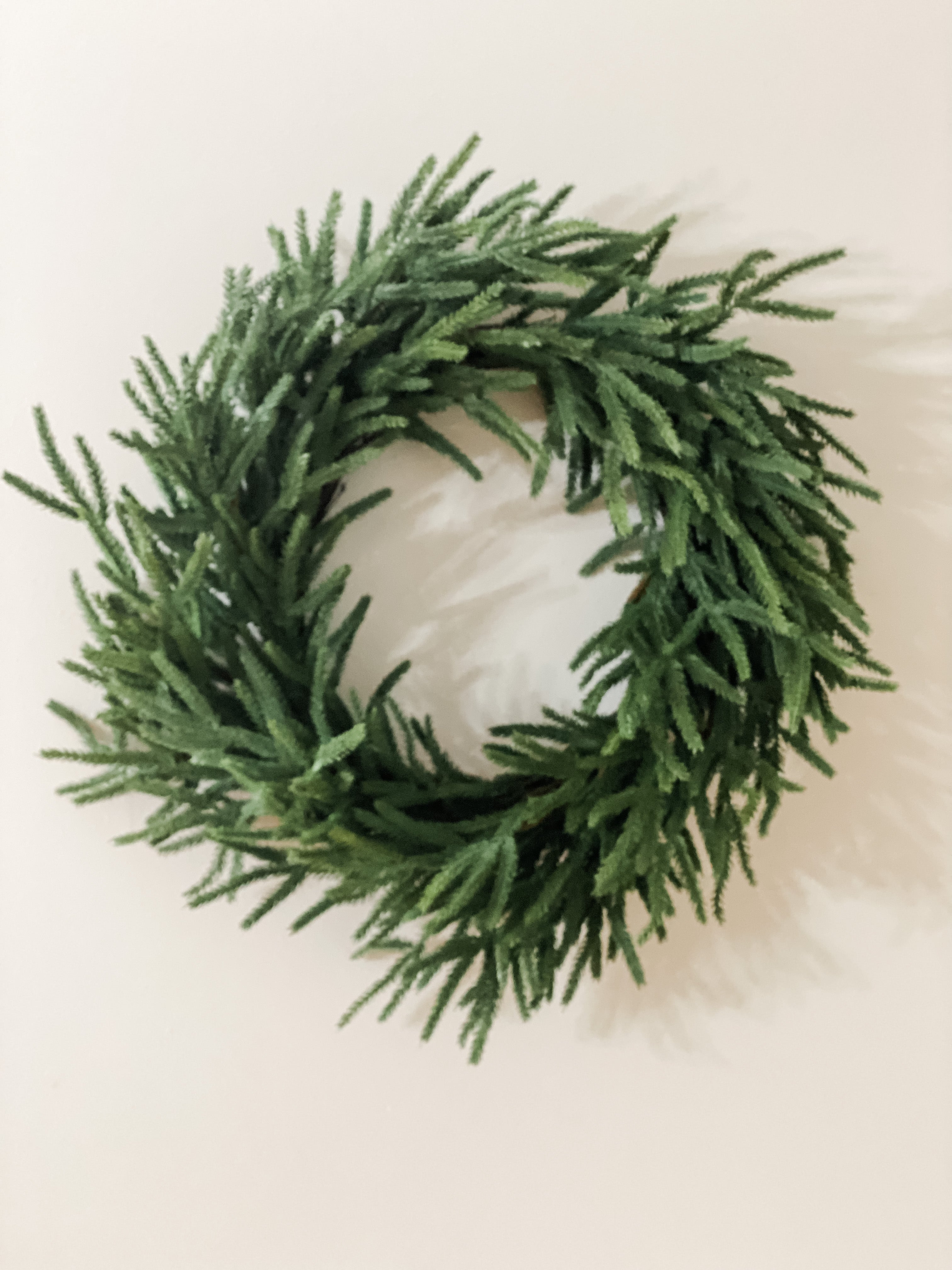 Lifelike Norfolk pine winter wreath with lush, textured green stems on a neutral background.