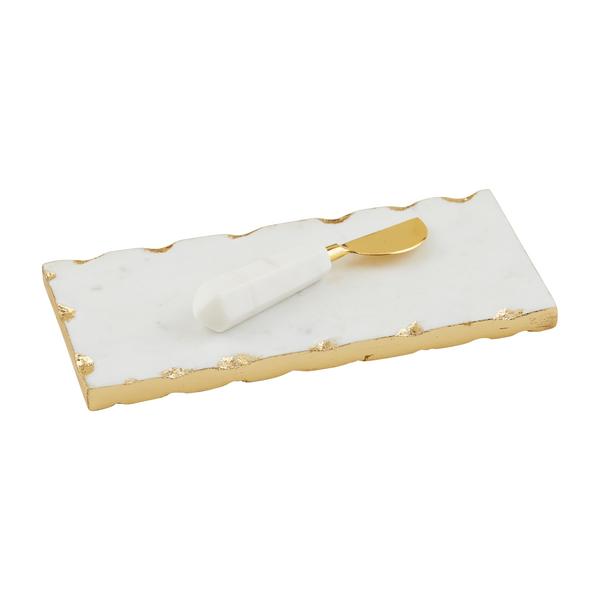 White marble serving board with gold foil raw edges and a matching marble-handled brass spreader.