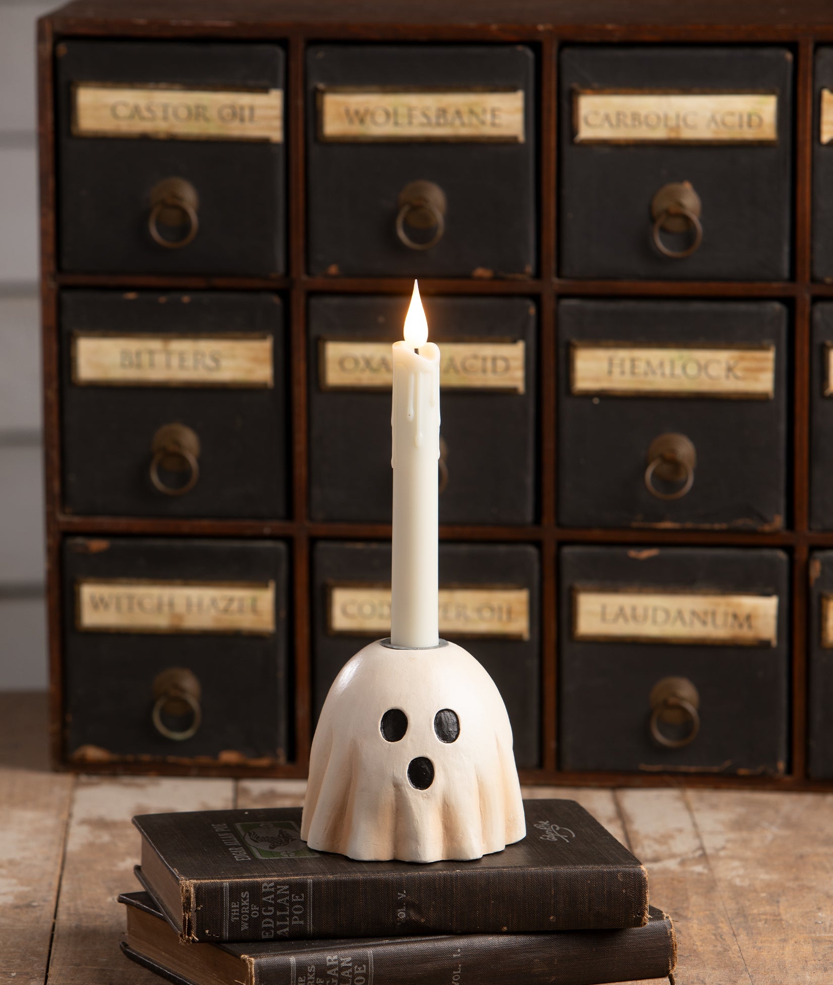 Bethany Lowe hand-painted resin surprised ghost candlestick holding a white taper candle on vintage books.